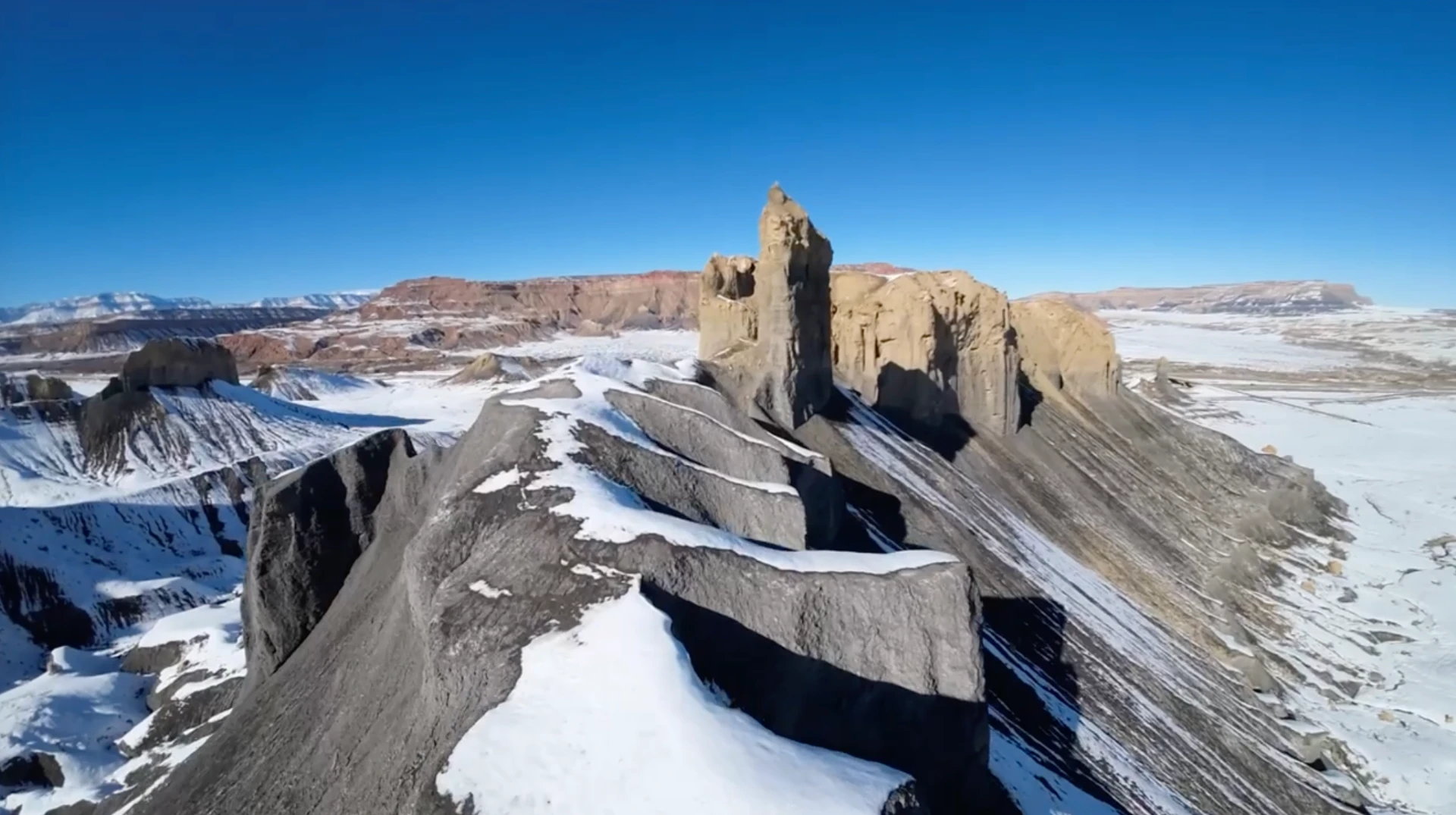 FPV drone flying over a rugged snowy desert landscape with dramatic rock formations